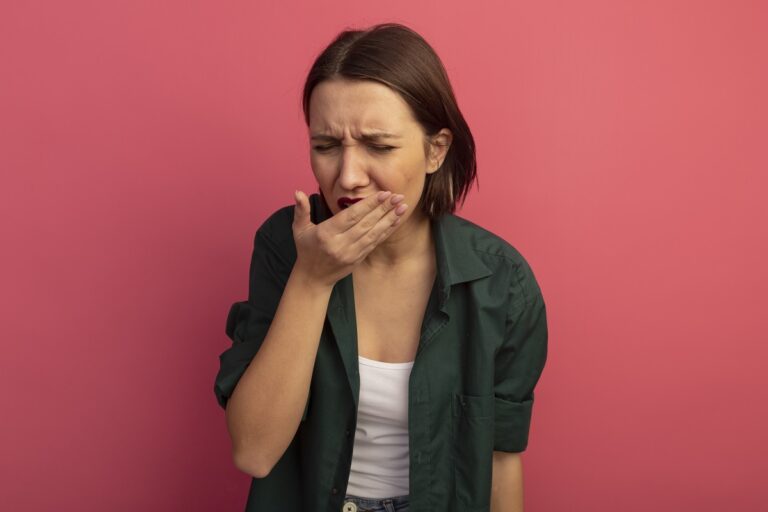 aching pretty caucasian woman puts hand on mouth isolated on pink background with copy space