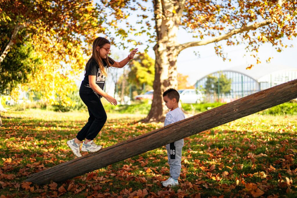 Copii de vârste diferite care se joacă împreună într-un parc, printre frunze de toamnă